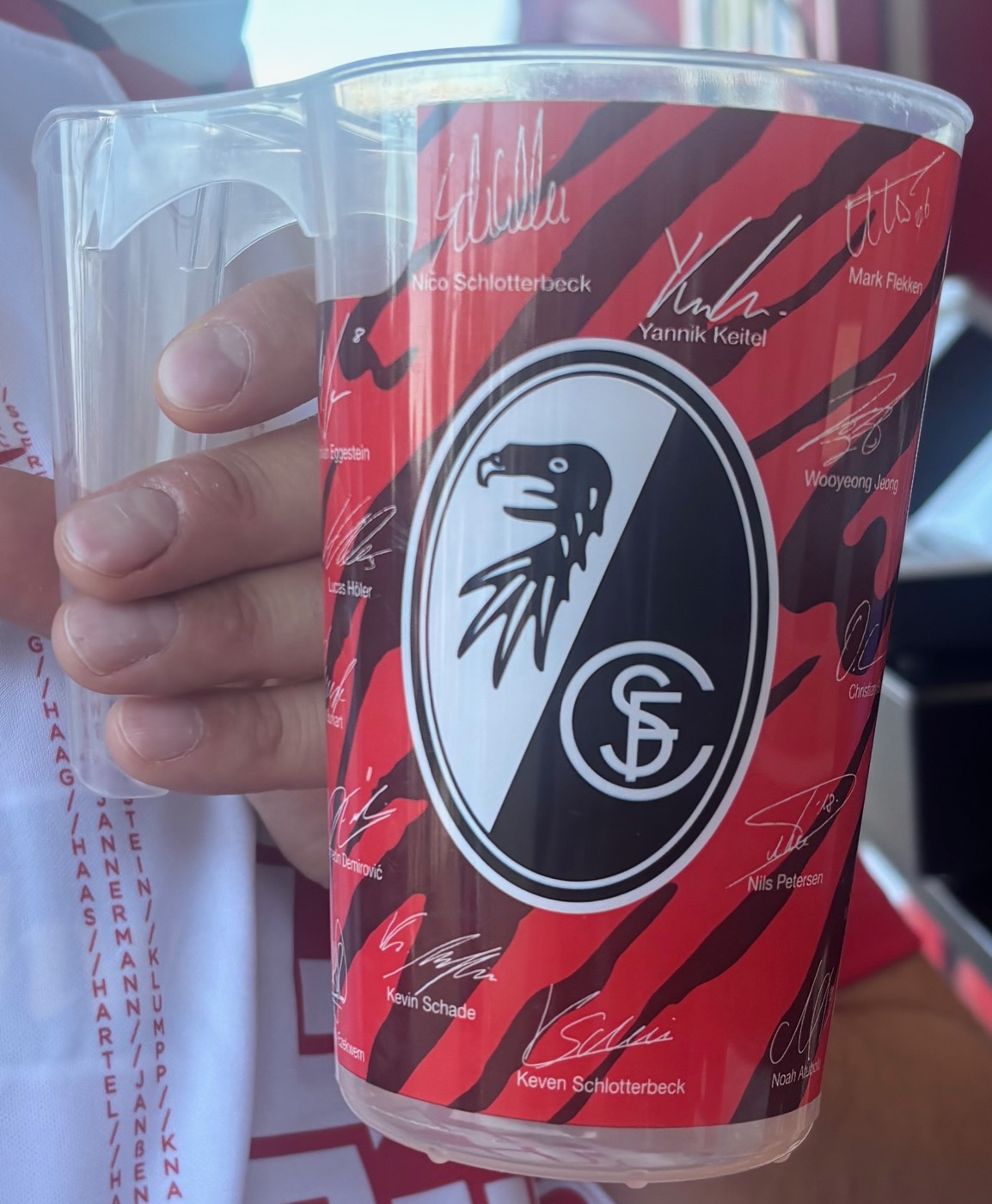 Signierter SC-Freiburg-Pfandbecher mit Vereinswappen und Unterschriften mehrerer Spieler.