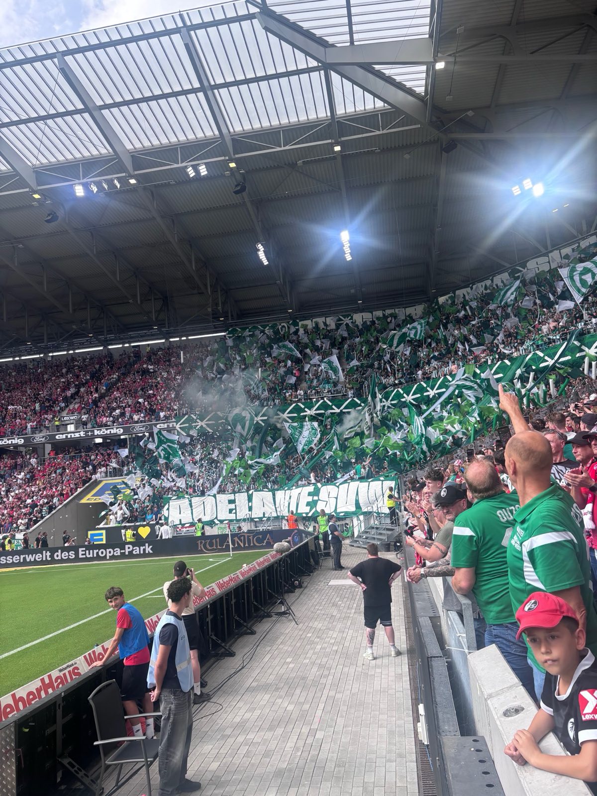 Werder-Gästeblock mit grün-weißer Fahnen-Choreo und dem Schriftzug 'Adelante SVW' im Europa-Park Stadion.