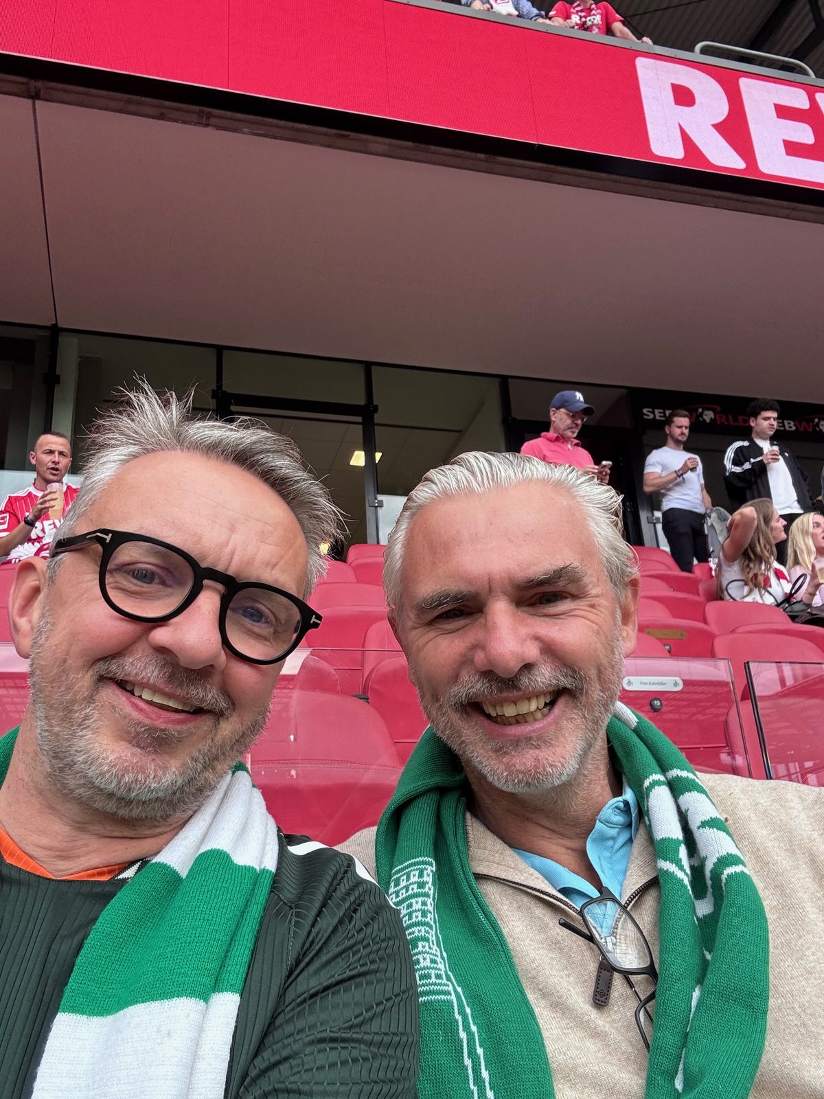 Selfie von zwei Männern mit grün-weißen Werder-Schals auf den roten Sitzen der Tribüne im RheinEnergieStadion.