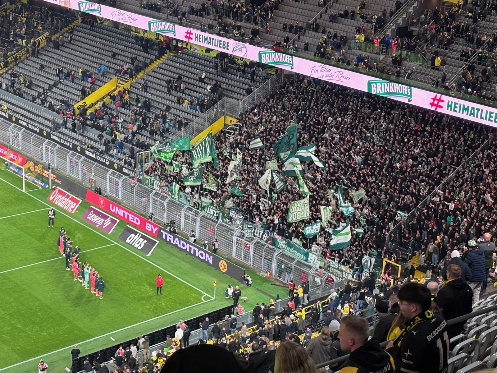 Nach dem Abpfiff stehen die Werder-Spieler in Pfirsich in einer Reihe auf dem Rasen vor dem Gästeblock im Signal Iduna Park, in dem die Fans grün-weiße Fahnen schwenken.